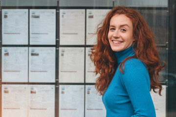 Smiling Woman With Red Hair Standing In Front Of Bulletin Board