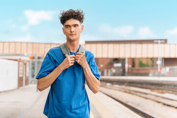 Young Man With Backpack Adjusting Straps on Train Platform