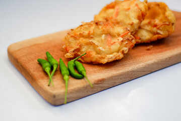 Top view of bakwan sayur or bala-bala or vegetable fritter, Indonesian snack made from flour, shrimps, cabbage, carrots and bean sprouts, served with green chili on wooden board