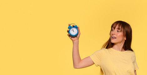 Woman Holding Blue Alarm Clock Against Yellow Background