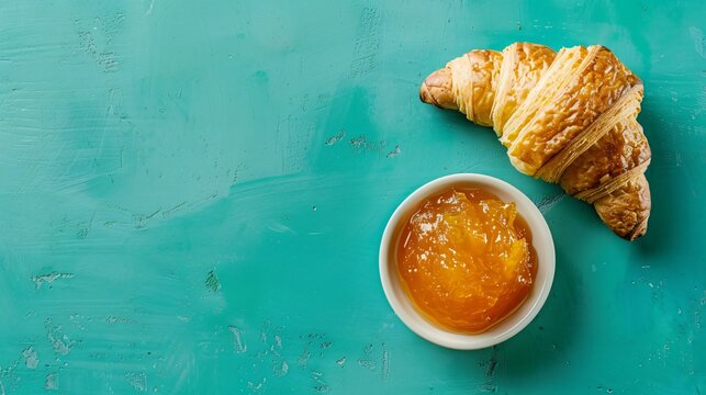 A croissant with a side of marmalade, against a vibrant turquoise background