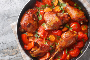 Delicious spicy rooster cooked with bell peppers, onions and carrots in tomato sauce close-up in a pan on the table. Horizontal top view from above