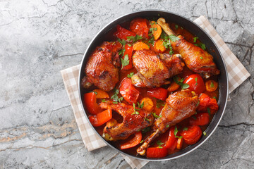 Homemade rooster stew with bell peppers, onions and carrots in a spicy tomato sauce close-up in a pan on the table. Horizontal top view from above