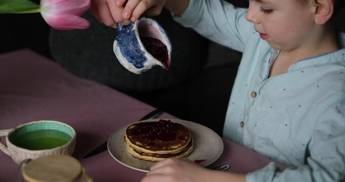 Little boy adorable having breakfast with pancakes with tea and apples at home. Cute weekend with sweet tasty food and emotional child. video footage 4k