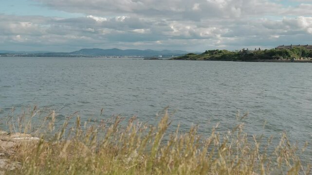 BURNTISLAND, FIFE, SCOTLAND, UK - JUNE 11, 2024: A peaceful view of the coastline in Burntisland, Fife, Scotland, with a cloudy sky overhead.