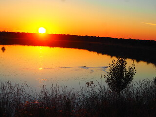 Obraz premium Sunset in hues of reddish-orange and yellow over the lake on a summer day.