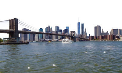 Daytime view of the Brooklyn Bridge and the Manhattan skyline, with boats on the water in foreground, clear skies