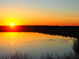 Sunset in hues of reddish-orange and yellow over the lake on a summer day.