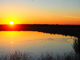 Fototapeta premium Sunset in hues of reddish-orange and yellow over the lake on a summer day.