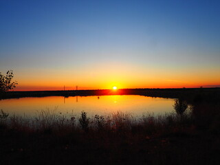 Obraz premium Sunset in hues of reddish-orange and yellow over the lake on a summer day.