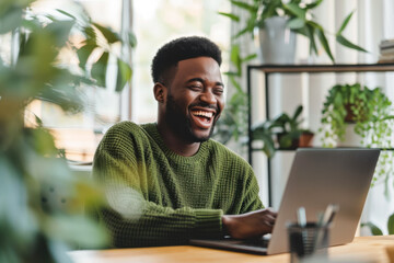 a man in an green sweater sits at his workplace next to a laptop and smiles
