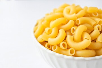 Raw uncooked macaroni in a white bowl on a white background, close up