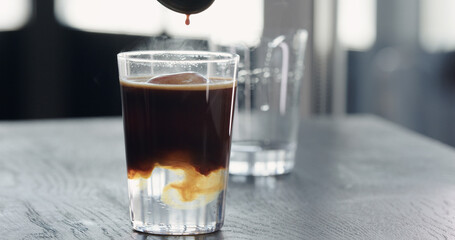 pour espresso into tonic with clear ice cube in tumbler glass on black oak table