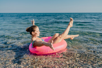 A woman is floating on a pink inflatable raft in the ocean