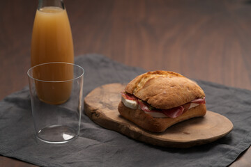 Sandwich with bresaola, mozzarella and pest on olive board with orange juice