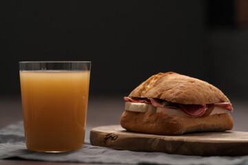 Sandwich with bresaola, mozzarella and pest on olive board with orange juice