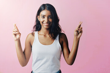 Studio, portrait and indian woman with fingers crossed for hope, trust and good luck for positive outcome for wish. Female person, hands and gesture of signal for sincerity, hope and pink background