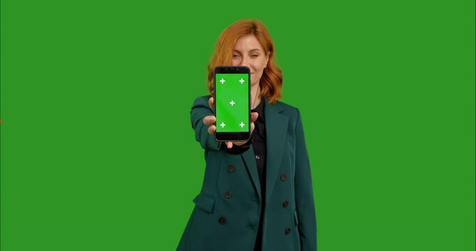 Business woman showing mock up smartphone to camera with smile over green screen background. New application star-up using smartphones. Chroma key background.