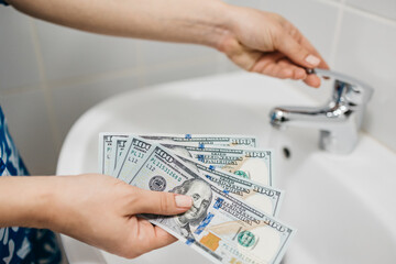 Women's hands hold money against the background of a sink and a faucet with water. Concept of utilities, payment and savings.