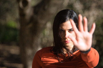 Portrait of a young, beautiful woman in an orange T-shirt, covering the camera with the palm of her...