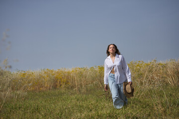 Young woman, farmer, beautiful, blonde, with green eyes, white shirt, jeans and hat, walking in the countryside, alone, free and empowered. Concept beauty, countryside, protection, peace, nature.