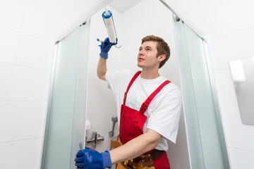 Young man repairing door of shower cabin in bathroom.