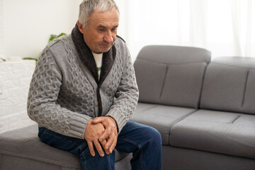 Old man suffering from knee pain sitting sofa