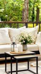 A white couch with pillows sits on a wooden deck with a bouquet of daisies in a vase and candles on a coffee table
