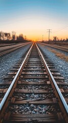 Fototapeta premium A pair of railroad tracks lead towards a setting sun in a rural landscape