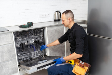 A plumber repairs a dishwasher in a kitchen room. Plumbing services. 