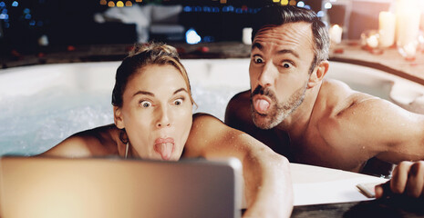 Tablet, funny face and selfie of couple in hot tub with tongue out for social media or romantic date. Technology, man and woman take picture in water to relax for vacation, holiday and memory at spa