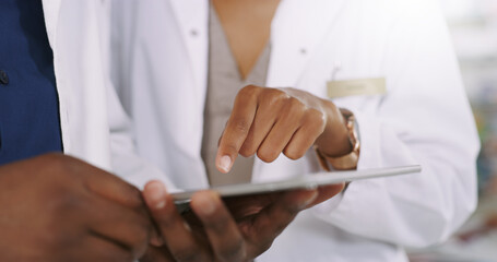 Pharmacist, hands and tablet with discussion for healthcare, medical study or research at pharmacy. Closeup of employees on technology for telehealth, inventory or checking online stock at dispensary