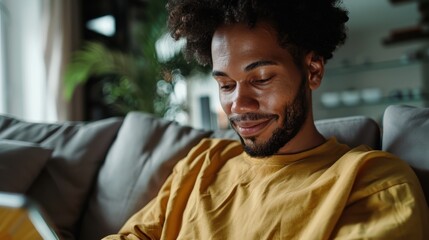 Young Man Relaxing on Sofa at Home, Smiling and Using Digital Tablet in Cozy Living Room