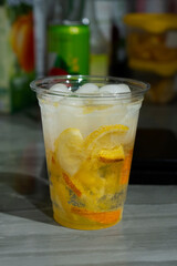 Cold lemonade with ice and fresh citrus pieces in a transparent plastic glass. Cold citrus mojito. Refreshing bright summer drink close-up.