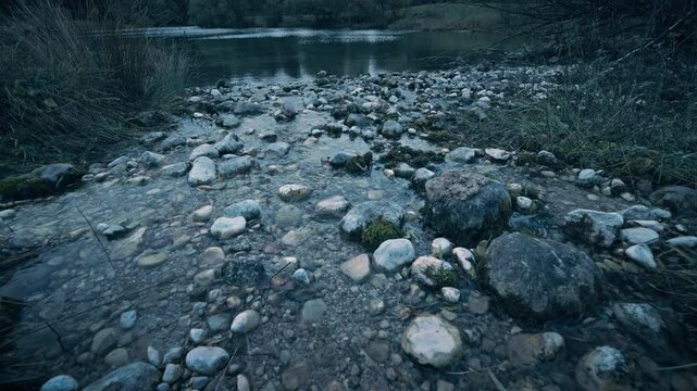 Water of a stream flowing through pebbles and rocks into a scenic lake, with moody cinematic blue toning. Tilting footage of a beautiful landscape in Bavaria, Germany 

