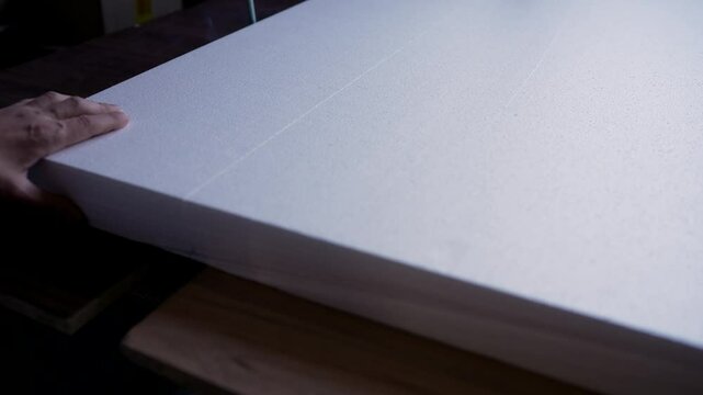A white sheet of foam plastic is cut with a hot wire. Polystyrene foam is cut using a hot wire. Cutting foam plastic for packaging goods.