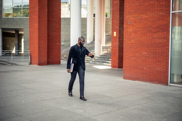 black African American businessman walking with laptop and checking watch in financial district