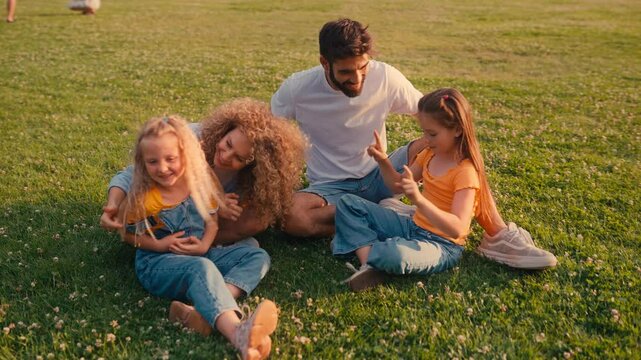 A happy family of parents and their two daughters enjoy playing in a sunny park filled with lush greenery, enhancing their bonding and creating joyful memories together