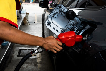 Fototapeta premium Attendant in uniform at the gas station, filling with petrol a small car, nozzle is in the tank