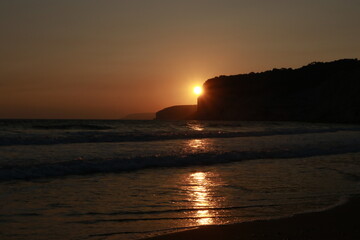 A serene beach scene at twilight. Gentle waves lap onto the shore, and the sky transitions from deep blue at the top to soft pink and orange hues near the horizon