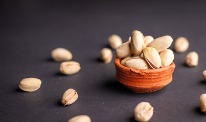 Pistachio nuts in wooden bowl on black background. Pistachios are rich in nutrients and good source of protein, fiber, and antioxidants. Healthy food concept. Flat layout.
