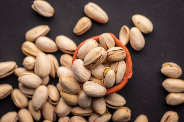 Pistachio nuts in wooden bowl on black background. Pistachios are rich in nutrients and good source of protein, fiber, and antioxidants. Healthy food concept. Flat layout.
