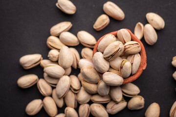 Pistachio nuts kept in a clay pot on a dark grey background