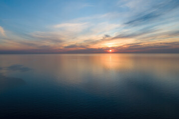 Aerial view of sunset over calm ocean waters with a distant horizon.