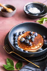 Pancake mit Heidelbeeren und Honig auf einem schwarzen Teller. Frühstück, servierfertig.