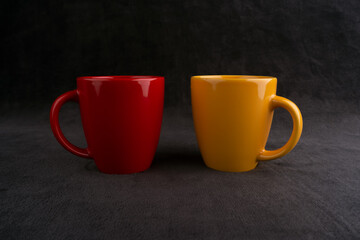 Coffee or tea cups on black texture background. Yellow mug. Red glass. Corporate colors. ceramic mugs