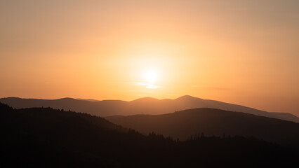 Sunset above horizon line with sun setting down behind mountains