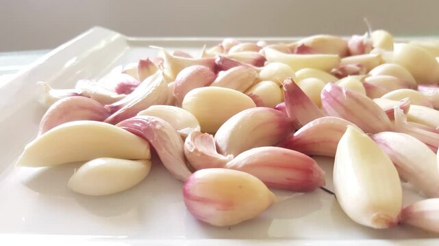Peeled garlic cloves on white stylish rectangular plate on horizontal pan shot