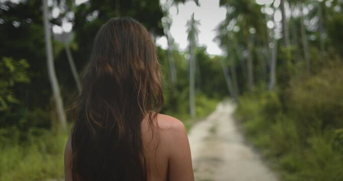 Beautiful long hair woman leisurely strolling jungle pam tree forest trail close up. Caucasian girl explore exotic island nature, relax, enjoy outdoor lifestyle travel on summer holiday vacation. Asia