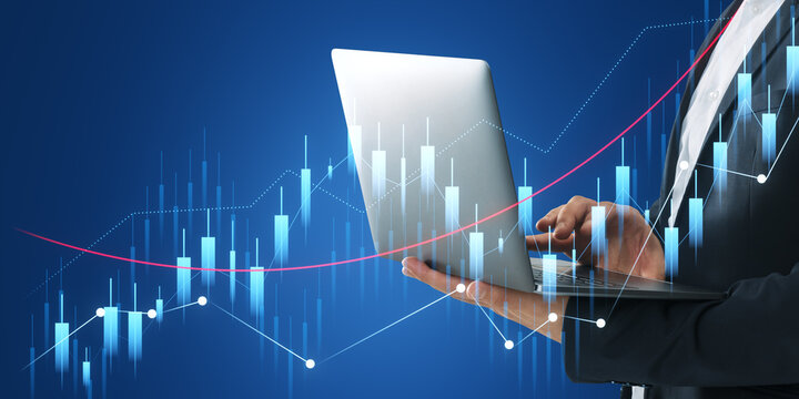 A person in a business suit holding a laptop, with futuristic financial graph holograms overlaid, on a dark blue background, depicting the concept of financial analysis